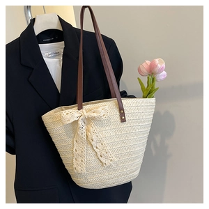Detail of woven straw tote bag with large lace bow and brown leather straps
