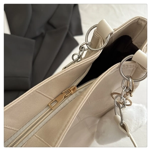 Detailed close-up of cream leather tote bag with gold zipper and plush ball charm