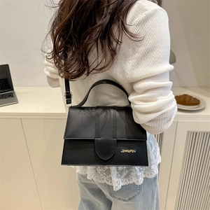 Sac à rabat noir minimaliste avec détails dorés porté par un mannequin en décor chaleureux
