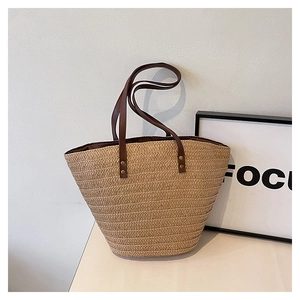 Detail of straw woven tote bag with brown leather handles and gold rivet accents