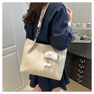 Detail of cream tote bag with geometric stitching, silver chain, and plush cloud charm