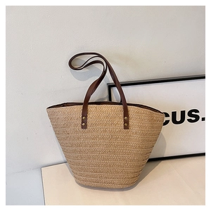 Close-up of beige woven straw tote bag with brown faux leather handles and gold rivets