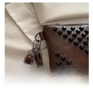 Close-up of silver metal hardware and black studs on a brown leather envelope handbag