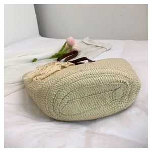 Detail of woven straw handbag with beige lace bow and dark brown leather handle