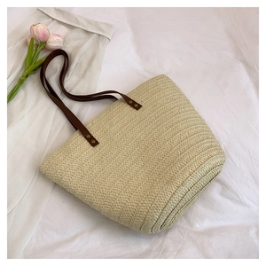 Detail of woven straw tote bag featuring brown leather handles and golden rivet accents