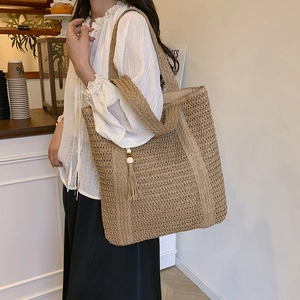 Handwoven straw tote bag with tassels shown on a model in a cozy cafe setting