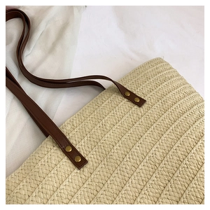 Detail of hand-woven beige straw tote bag with brown leather strap and gold metal rivets