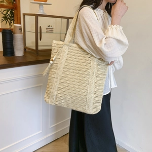 Handcrafted woven straw tote bag with beaded tassel charm on a model's shoulder