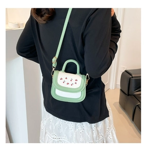 Detail of sweet green contrast mini bag with cherry print on model in casual indoor setting