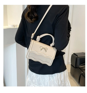 Detailansicht einer Frau mit cremefarbener Tasche mit Wellenklappe und Schleifendetail