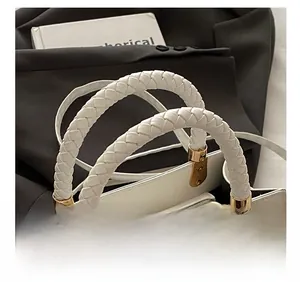 Close-up of a white fashion bag featuring a woven handle and gold-tone metal buckles