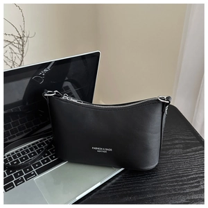 Detail of black minimalist bucket bag with silver zipper on a desk with laptop