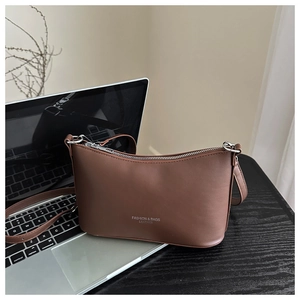 Detail of a brown leather bucket bag next to a laptop showing the sleek matte texture