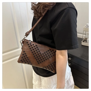 Close-up of brown leather shoulder bag with V-shaped rivet studs on adjustable strap