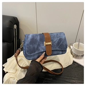 Détail du sac baguette en denim bleu avec bandoulière en cuir brun et boucle dorée