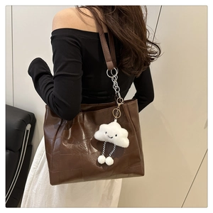 Detail of dark brown leather tote bag with chain strap and white plush cloud charm