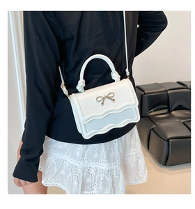 Detail der weißen Tasche mit Wellenkante, goldener Schleife und gedrehtem Tragegriff