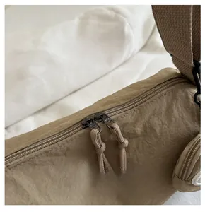 Close-up of smooth dual zippers and nylon texture on a large khaki crossbody bag