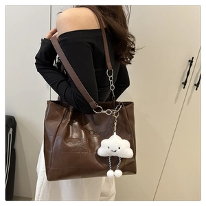 Macro view of dark brown tote bag with geometric texture and plush cloud charm detail
