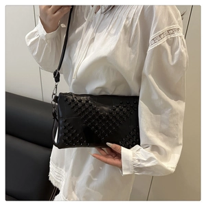 Detail of a black studded crossbody bag worn as a shoulder purse with metallic rivets