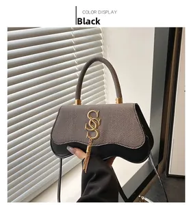Détail d'un sac bandoulière chic noir et beige avec logo S doré et pompon à franges