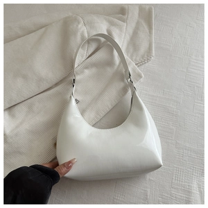 Gros plan d'un sac baguette en cuir verni blanc brillant sur un tissu à carreaux beige
