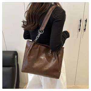 Detail of dark brown leather tote bag with irregular patchwork and silver chain strap