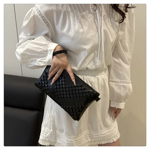 Detail of black leather clutch bag with matte rivets and wristlet strap on white outfit