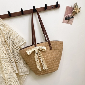 Straw woven tote bag with brown leather straps and a delicate white lace bow decoration