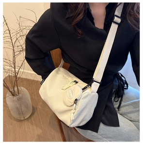 Close-up of cream white cylindrical crossbody bag featuring a woven adjustable strap