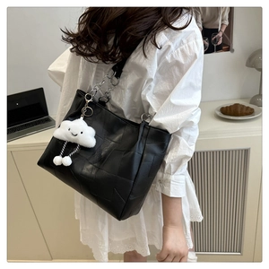 Detail of a black patchwork tote bag with silver chain strap and a white cloud charm