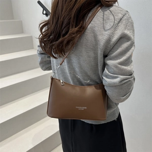Brown leather bucket bag with white lettering shown on a model against a white staircase