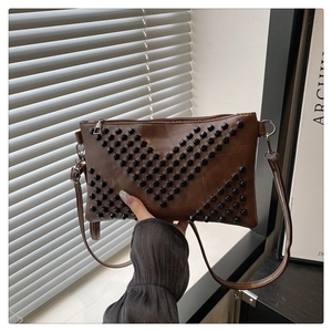 Detail of dark brown leather envelope bag with V-shaped punk rivets and long shoulder strap