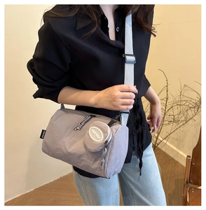Close-up of grey cylindrical shoulder bag with textured nylon and mini pouch charm