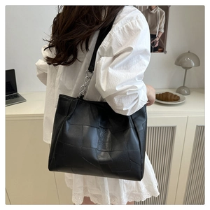 Detail of black leather tote bag with geometric stitching and silver chain strap