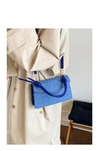 Détail d'un élégant sac à main en tissu bleu porté avec un trench-coat kaki