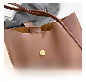 Detail of a brown leather tote bag with a secure magnetic button closure design