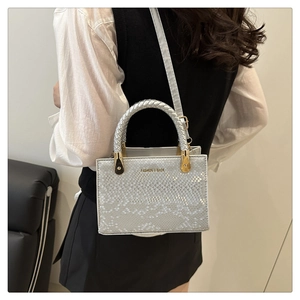 Detail of silver snake-pattern crossbody bag with woven handle and gold hardware accents