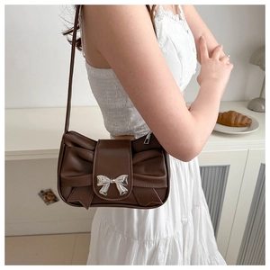 Detailed view of brown ruched underarm bag with silver bow buckle on model