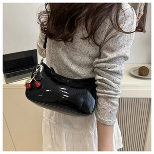 Close-up of glossy patent leather shoulder bag with cherry charm and chain detail