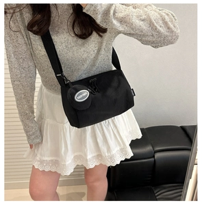 Detail of a black nylon shoulder bag with a small detachable coin purse and woven strap