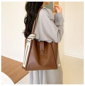 Detail of brown tote bag with wide canvas shoulder strap and gold bottom metal studs