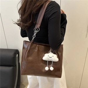 Retro dark brown tote bag with chain strap and plush charm worn by a model