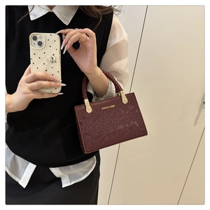 Detail of burgundy snakeskin embossed crossbody bag with woven handle and gold accents