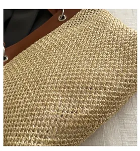Detail of straw woven tote bag with brown faux leather trim and silver metal eyelets