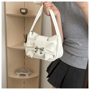 Close-up of white pleated handbag featuring silver bow clasp and elegant ribbon details