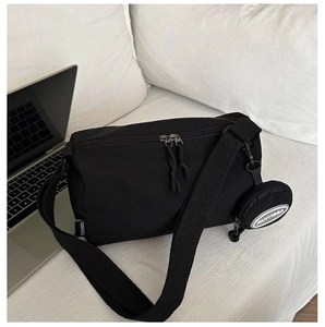 Detailed view of black nylon crossbody bag with detachable round coin purse on sofa