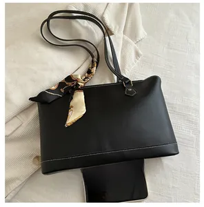Close-up of black leather tote with white stitching and decorative silk scarf