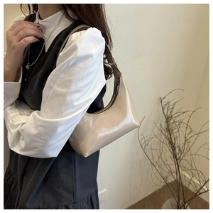 Détail d'un sac hobo en cuir verni beige porté par un mannequin dans un cadre minimaliste
