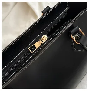 Detailed macro view of the smooth gold metal zipper and white stitching on black leather tote